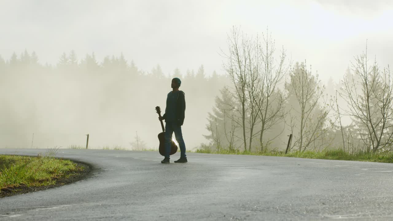 Person walking on a foggy road with a guitar