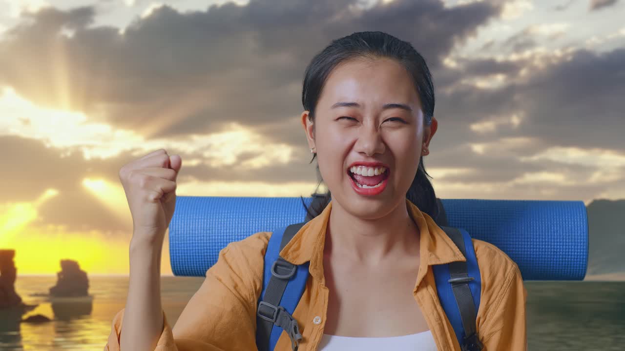 登山用バックパックを背負い、夕暮れ時のビーチに立って成功を叫び、喜ぶアジア人女性ハイカーのクローズアップ