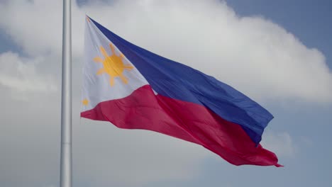 gran bandera filipina ondeando en el viento contra un cielo parcialmente nublado mientras está en un gran mástil de bandera en 4k en cámara lenta