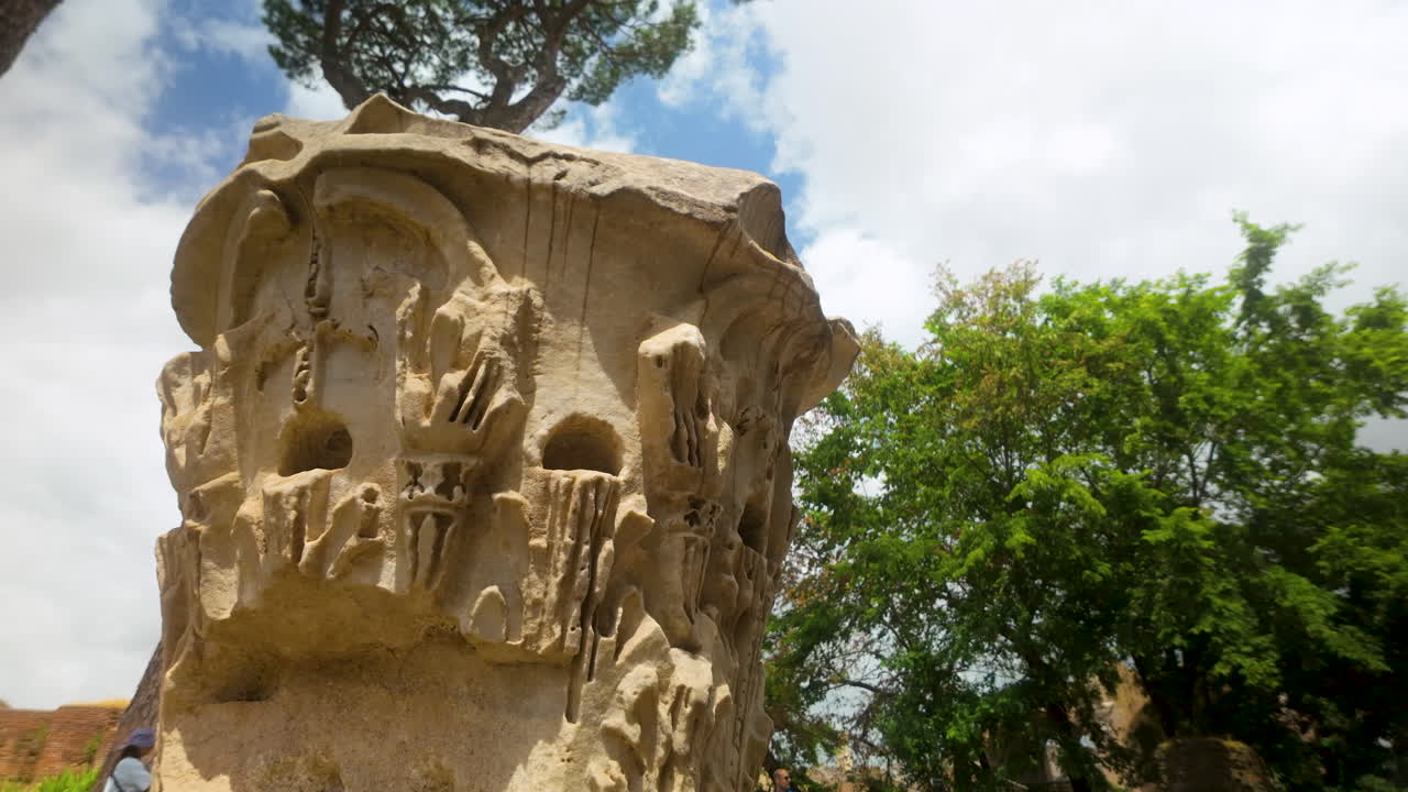 Decorated capital of ancient Roman column with trees in background