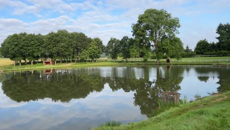 Cielo-Azul,-Nubes-Y-Reflejos-De-árboles-En-Un-Lago-Tranquilo.