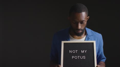 Portrait-Of-Man-Holding-Not-My-POTUS-Sign-In-Election-Against-Black-Background