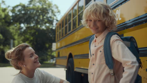 mom giving son five at school transport close up. boy get in yellow schoolbus.