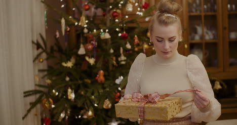 Curious-Woman-Holding-Christmas-Present-At-Home