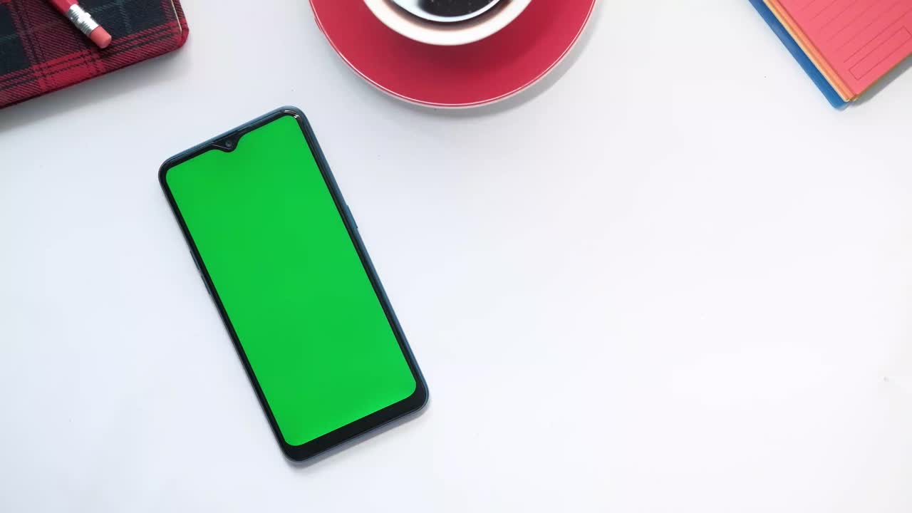 persona tocando un teléfono inteligente con pantalla verde en un escritorio con café y suministros de oficina