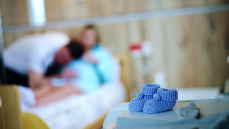 little blue knitted socks prepared for newborn. couple expecting child at backdrop in blur.