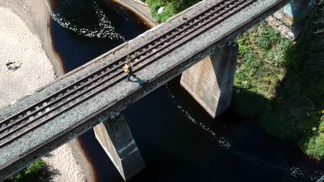 drone shot of man walking on traintracks with a strean underneath the bridge in canada