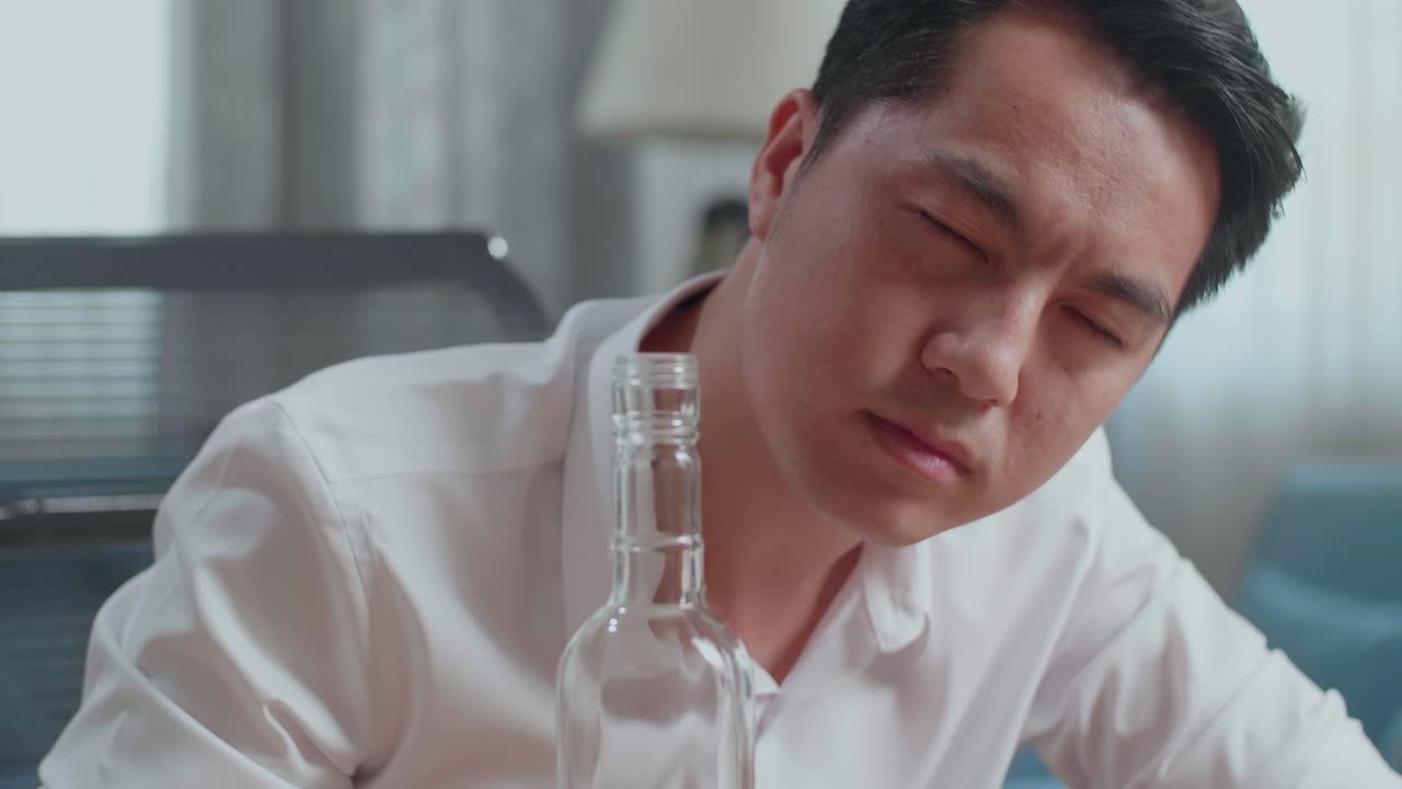 술에 취한 아시아인 남자가 보드카를 마시며 집에서 카메라를 쳐다보고 있다.