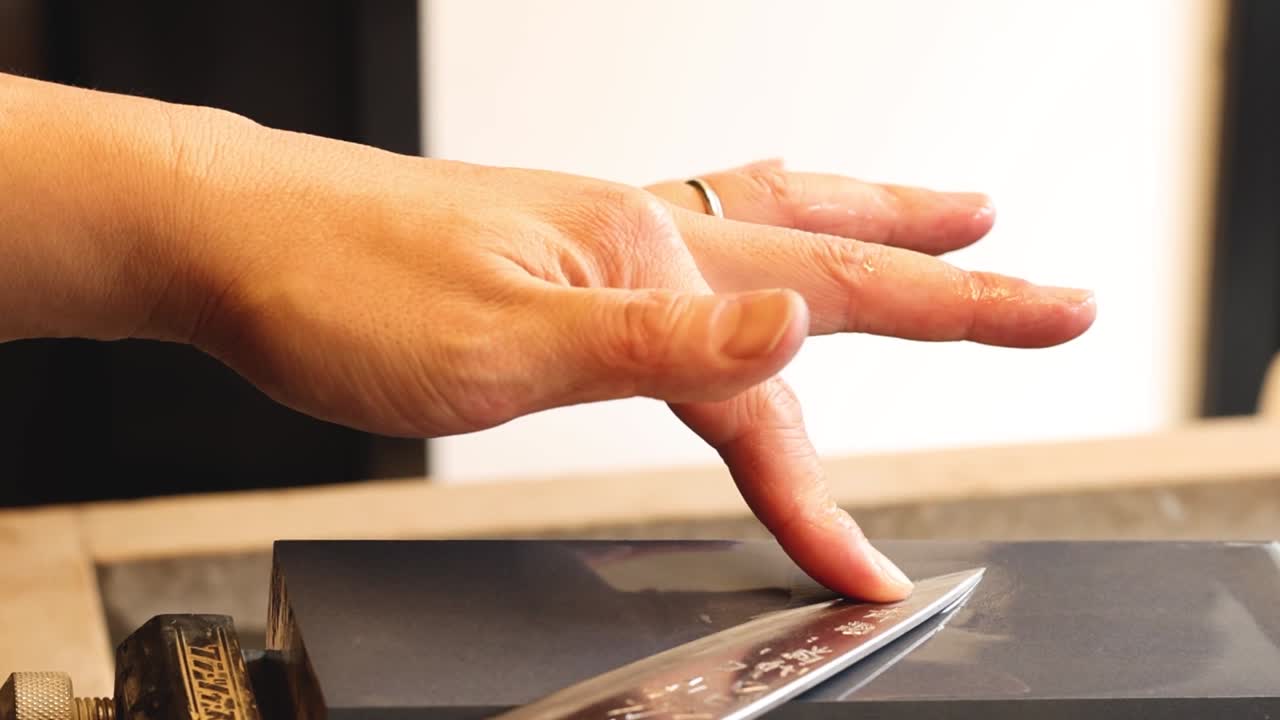 Detailed view of hands carefully honing a metal blade on a professional sharpening stone