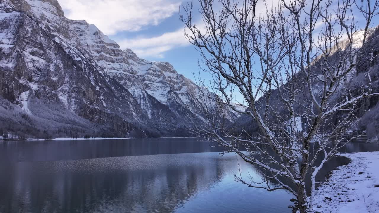 Lake Klöntalersee captured by a drone on a winter day in the Swiss Alps, surrounded by snow-covered landscapes.