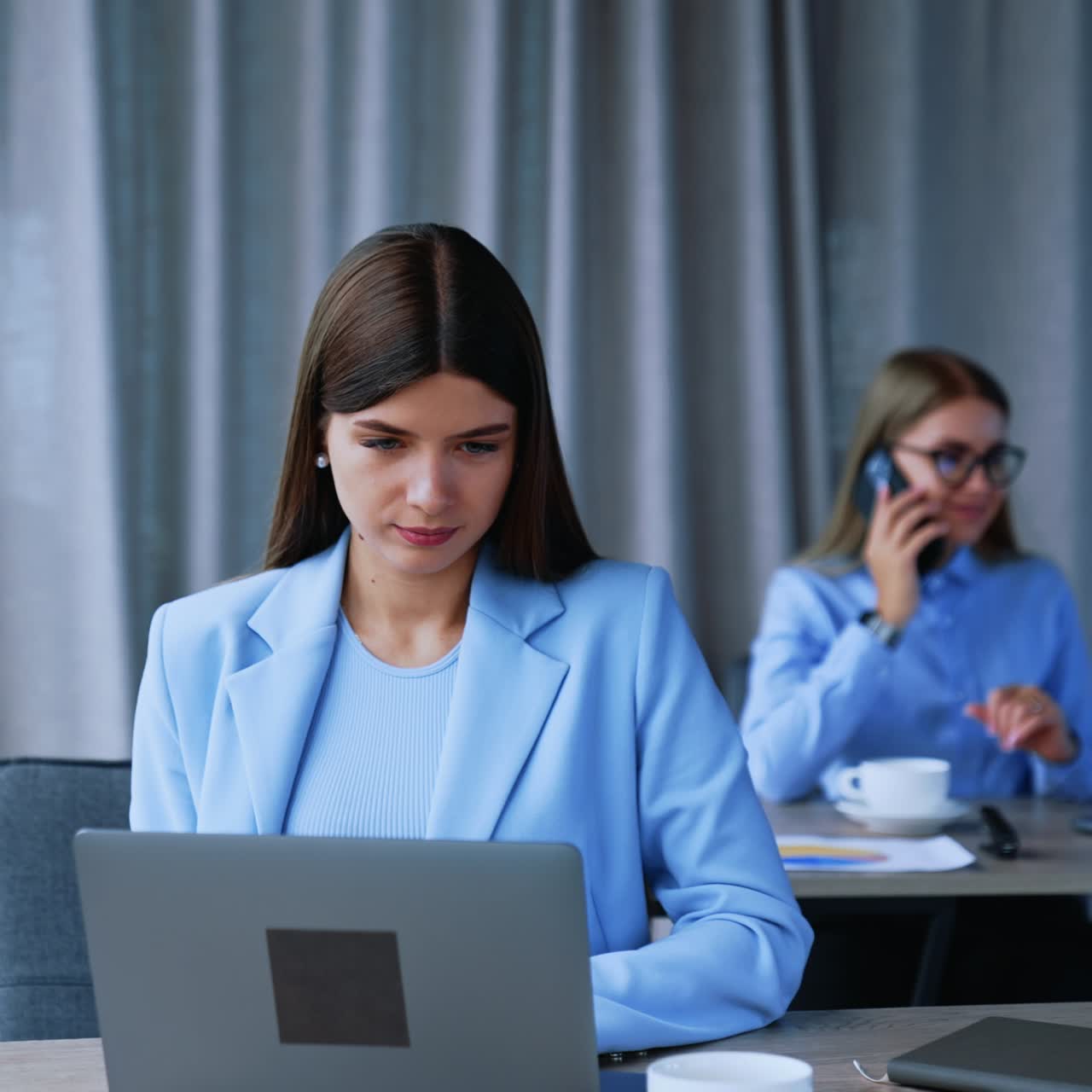 Women working at the modern office. Long-haired female employees sitting at the desks using laptops at their work