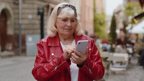 Senior woman use smartphone typing text messages browsing internet finishing work looking at camera