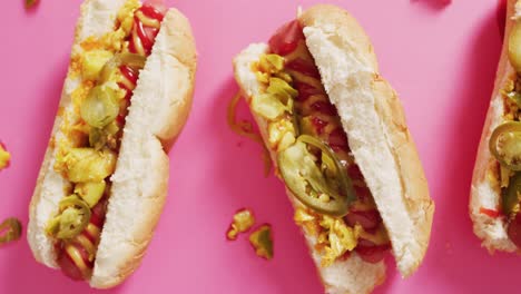 video of hot dogs with mustard, ketchup and jalapeno on a pink surface