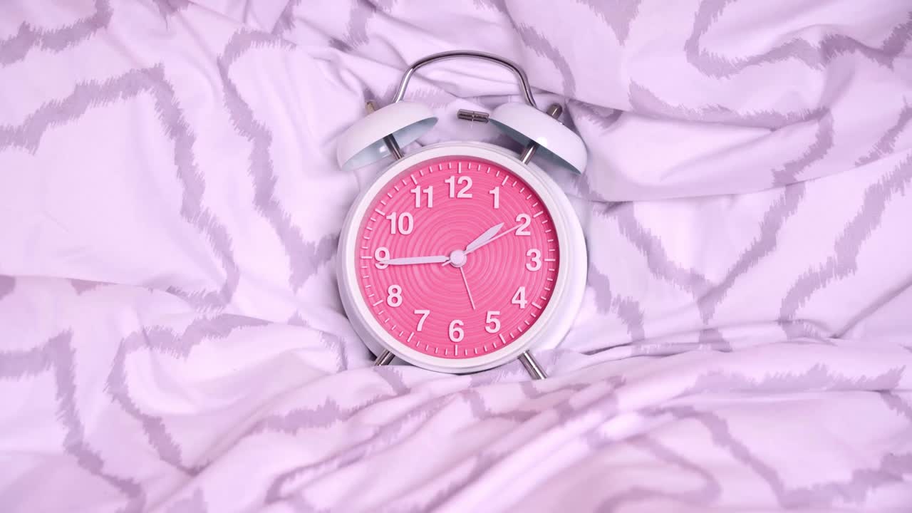 Timelapse of a cute old-fashioned alarm clock on modern bed sheets