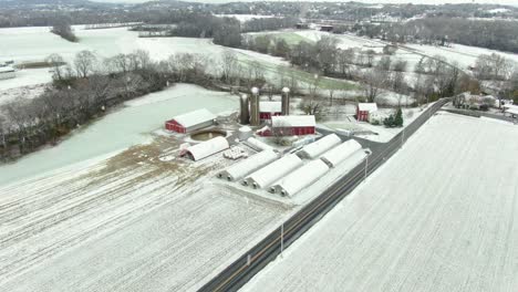 aerial of rural family farm in usa with red buildings and barns during snow storm