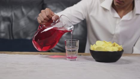 closeup of man pouring red beverage into glass with crisps, static