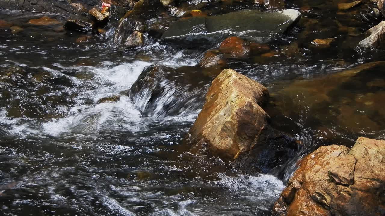Acqua cristallina e fresca di cascata montana e del fiume Crocodile, scintillante e che scorre su rocce e ciottoli, nei giardini botanici nazionali Walter Sisulu a Roodepoort, Sudafrica