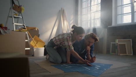 Focused-woman-and-young-man-speaking-about-home-repair-scheme-on-floor.