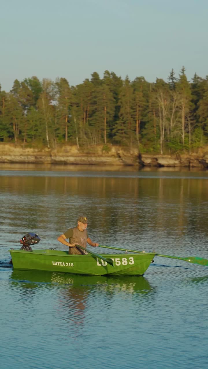 Vertical video of senior men rowing a boat upstream in the river.
