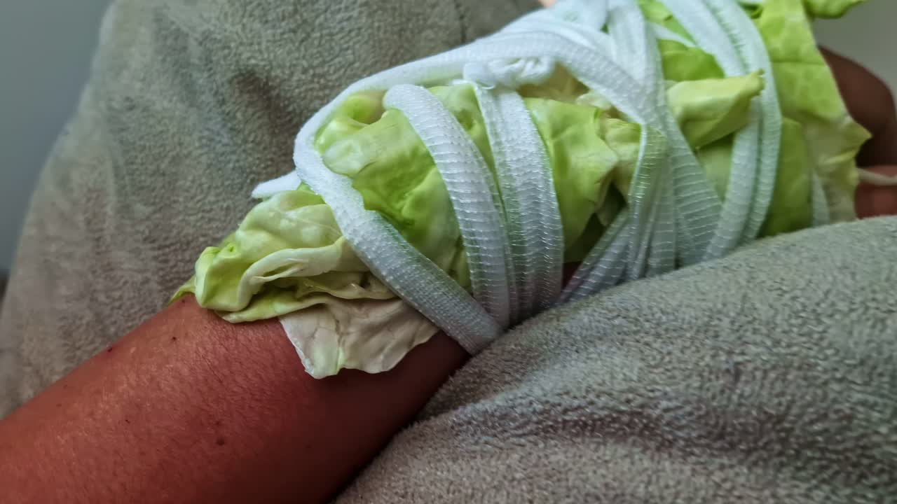 Someone's hand is wrapped or bandaged with lettuce and has a pain-relieving effect