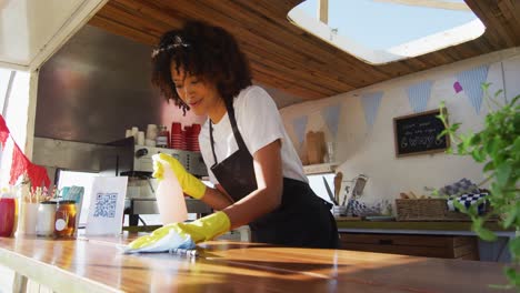 Mujer-Afroamericana-Con-Delantal-Y-Guantes-Limpiando-El-Camión-De-Comida-Con-Spray-Desinfectante