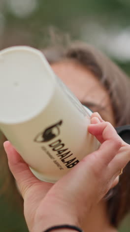 close-up of a smiling woman drinking water from a white water bottle, enjoying refreshment during outdoor activity, promoting hydration, wellness, and healthy lifestyle choices
