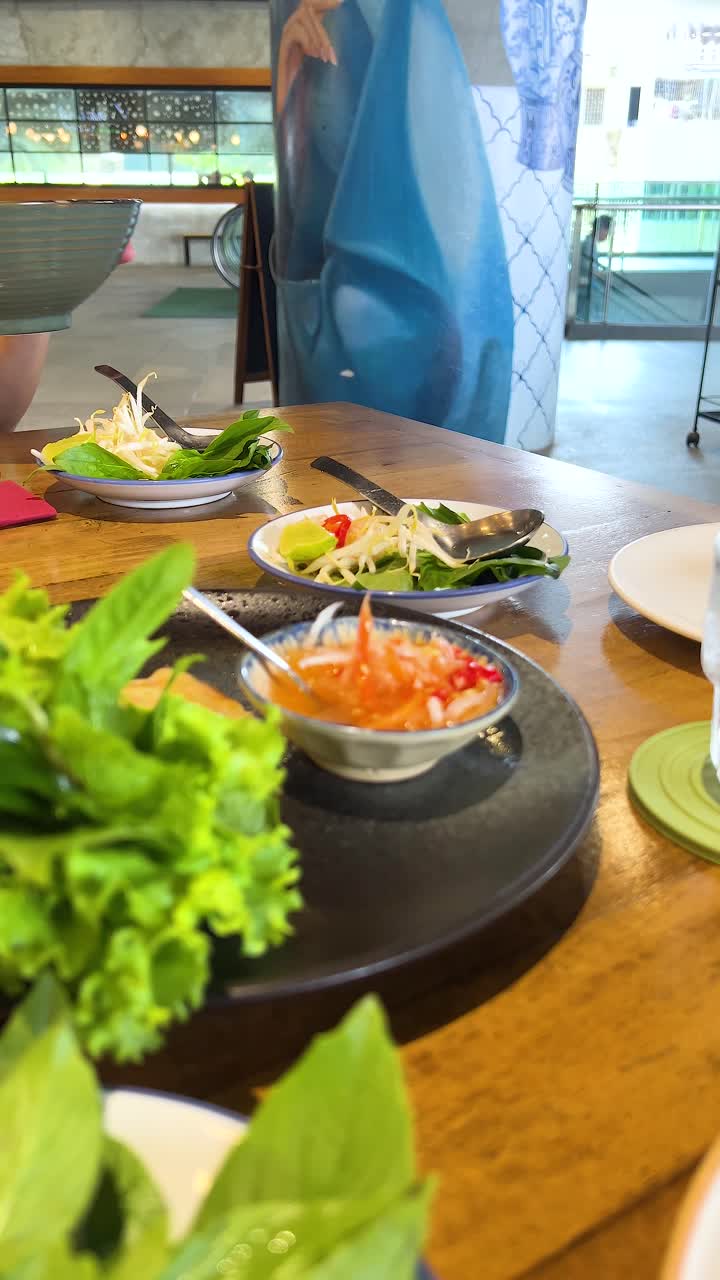 Dos personas disfrutan de la cocina vietnamita en un restaurante bien iluminado, destacando ingredientes frescos y colores vibrantes.