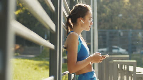 side view of a a pretty sportswoman texting message on smartphone and laughing at outdoor court on a summer day