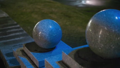 side view of three illuminated granite spheres at night, showcasing their smooth, polished surfaces and the soft, blue lighting