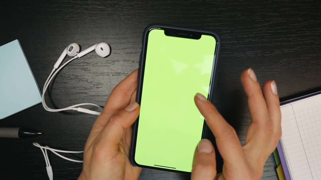 teléfono con pantalla verde en las manos. espacio de copia de pantalla chromakey. manos de persona sosteniendo teléfono inteligente con pantalla verde sobre el fondo de la mesa, deslizando y desplazándose