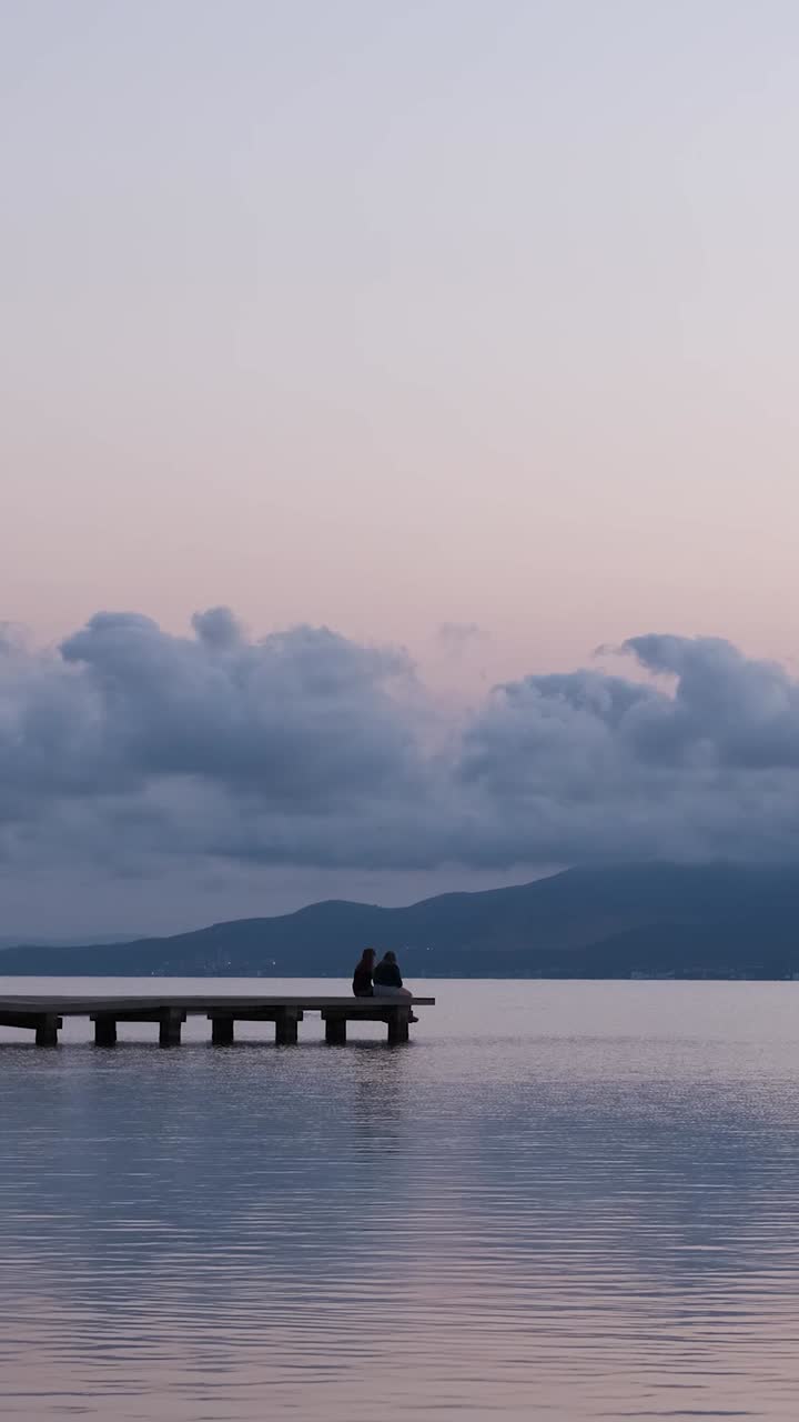 Unrecognizable persons relaxing on quay near sea in evening under sundown sky in summer