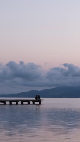 unrecognizable persons relaxing on quay near sea in evening under sundown sky in summer