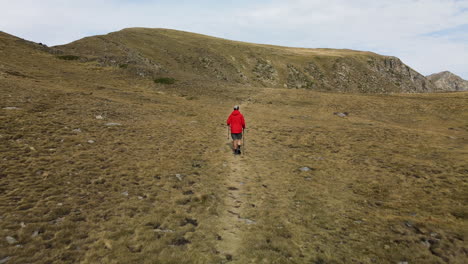 hiker on a red coat following the path in the mountains leading to an astonishing mountain range