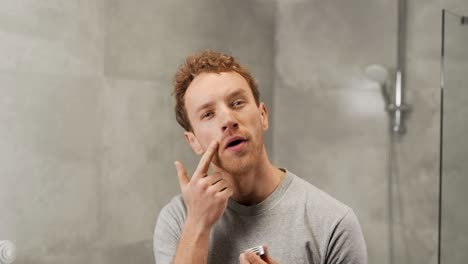 curly-handsome-man-applies-cream-on-face