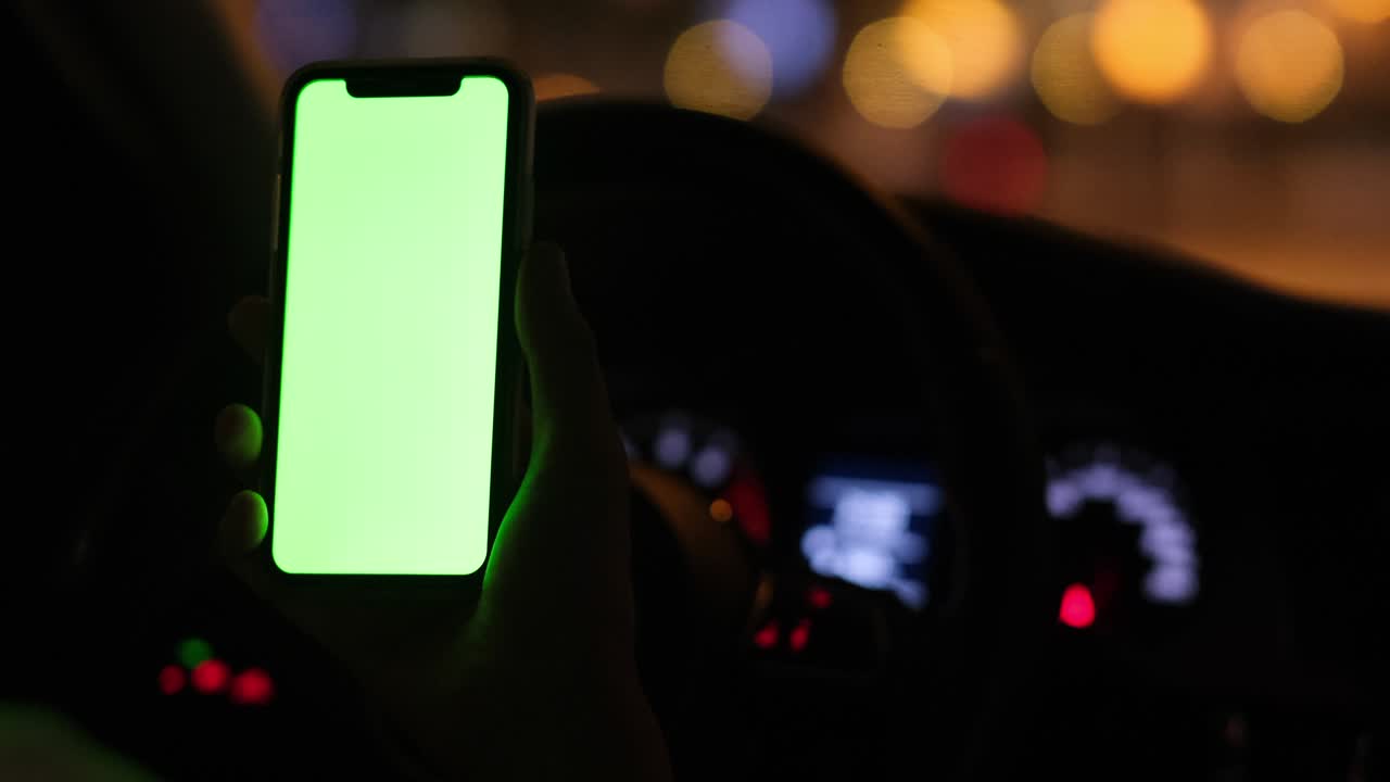 hand holding green screen phone in car at night