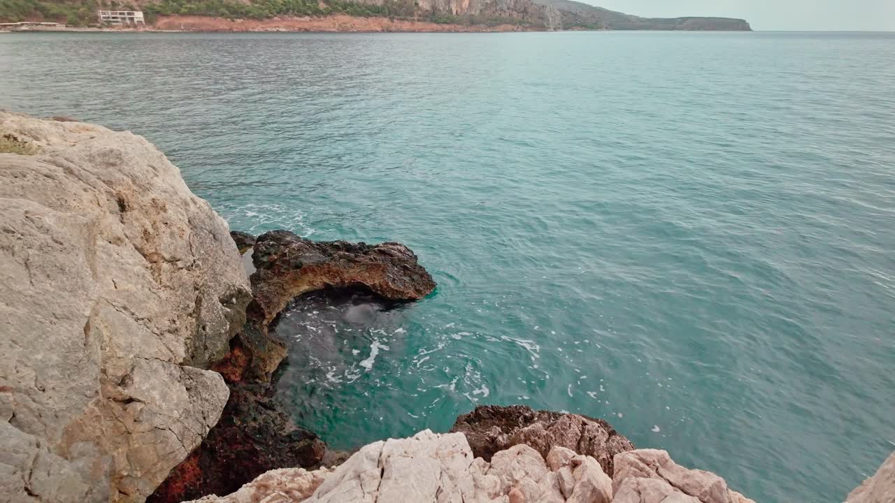 Beautiful clear azure sea waves splash against rocky coastal shore