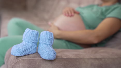 pregnant woman with a big belly, tummy, laying at the sofa with knitted shoes for the baby. happy pregnancy, family, parenting, motherhood concept