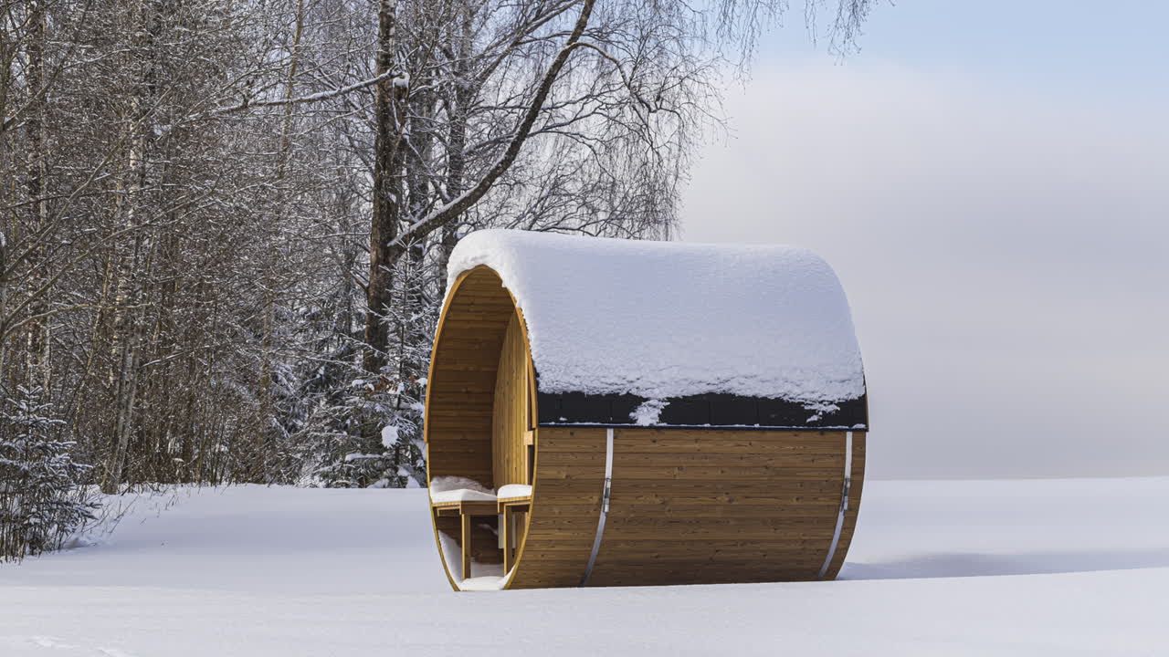 Sauna a botte in Thermowood innevata durante la stagione invernale vicino a un bosco