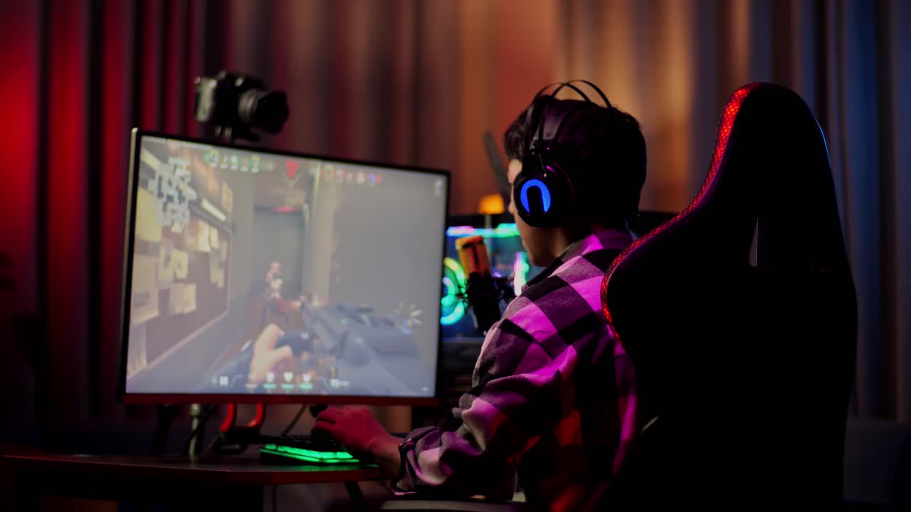 vista trasera de un niño asiático que grita gol celebrando el juego ganador a través de la red en una computadora personal. videojuego de transmisión en vivo, escritorio iluminado por luz de tira led rgb