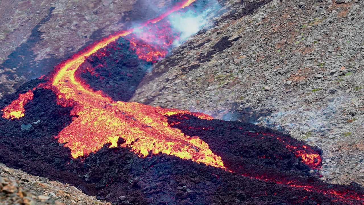 toma amplia que muestra lava fundida arrastrándose sobre una superficie áspera de basalto oscuro