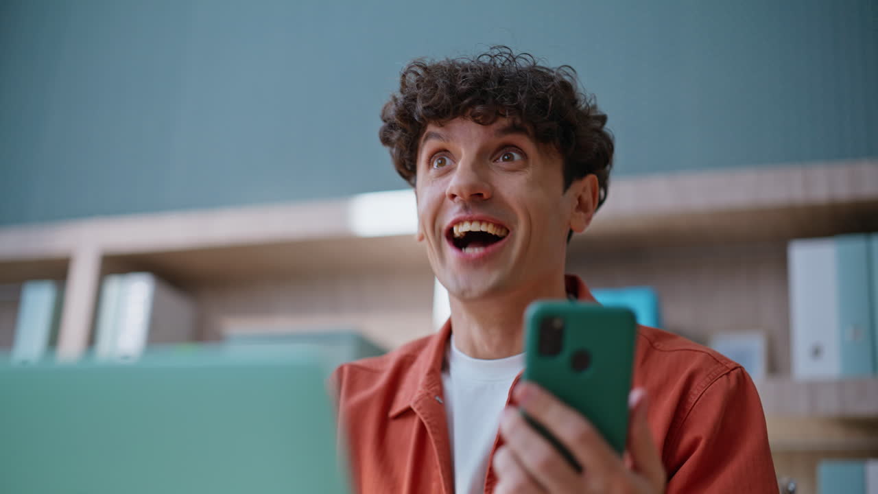 Primo piano di un dipendente felicissimo che celebra il successo guardando lo smartphone dopo aver scritto un messaggio