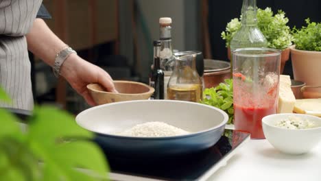 cook pouring rice into pan while preparing dish