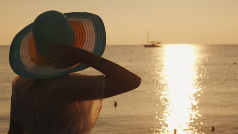 Una-Mujer-Joven-Se-Encuentra-Con-El-Amanecer-En-El-Muelle,-Se-Sienta-Y-Mira-El-Sol-Y-El-Barco-En-El-Mar-Dre