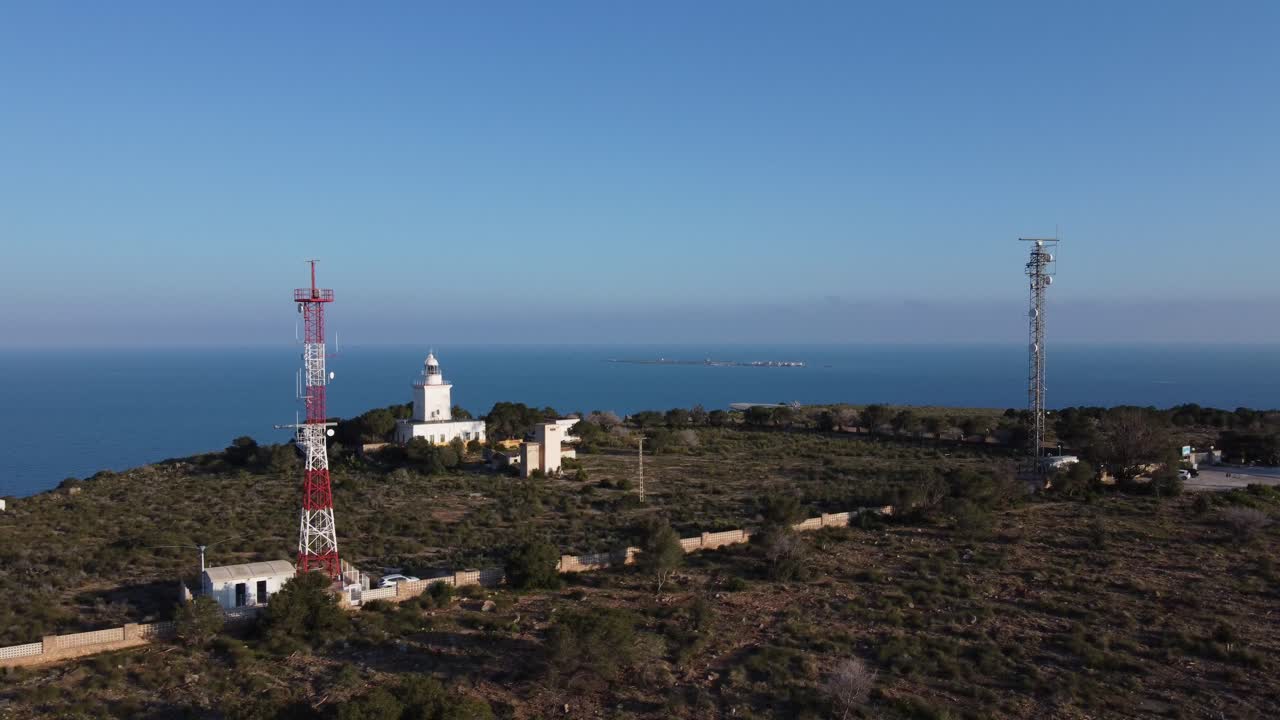 Statisk luftfoto af et fyrtårn og kommunikations- og detektionsantenner, med havet i baggrunden. Santa Pola, Spanien. Tabarca-øen i baggrunden.