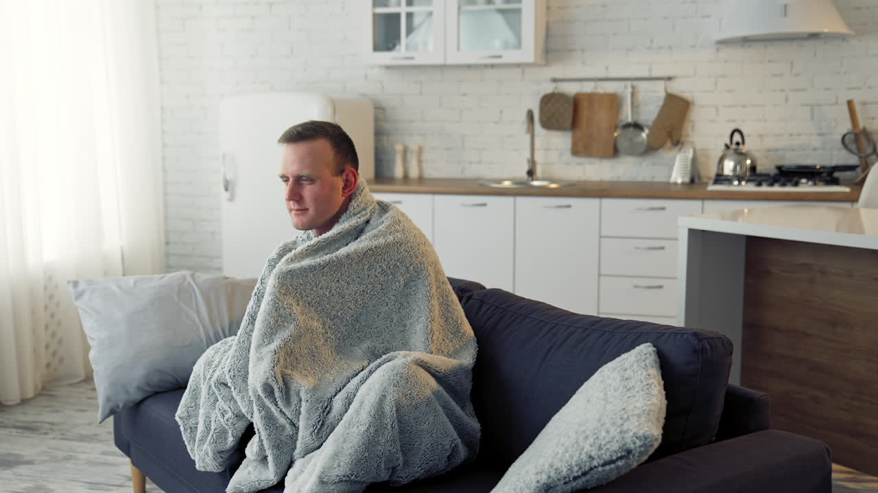 Unwell guy suffering coronavirus infection. Sick man with feeling ill and laying down on bed wrapped in blanket.