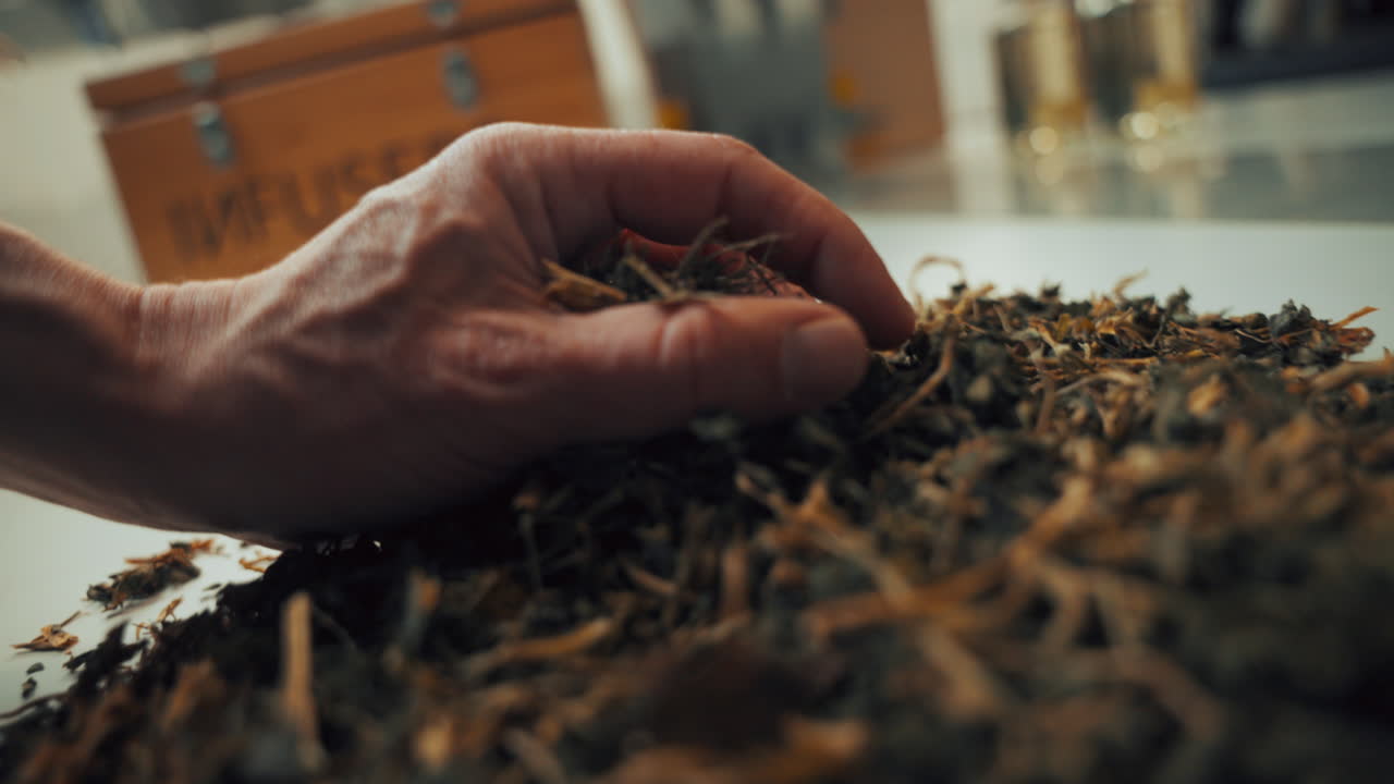disparo de cerca de una mano masculina recogiendo hierbas aromáticas secas de especias de una mesa blanca
