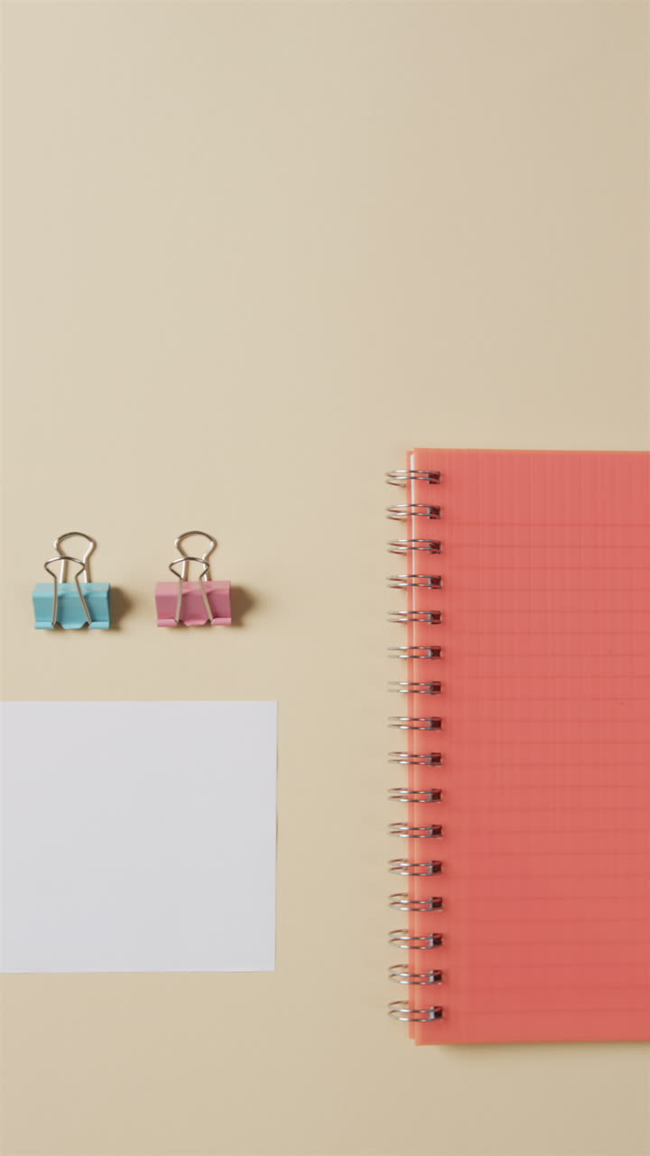 Vertical video of overhead view of school stationery on beige background, in slow motion