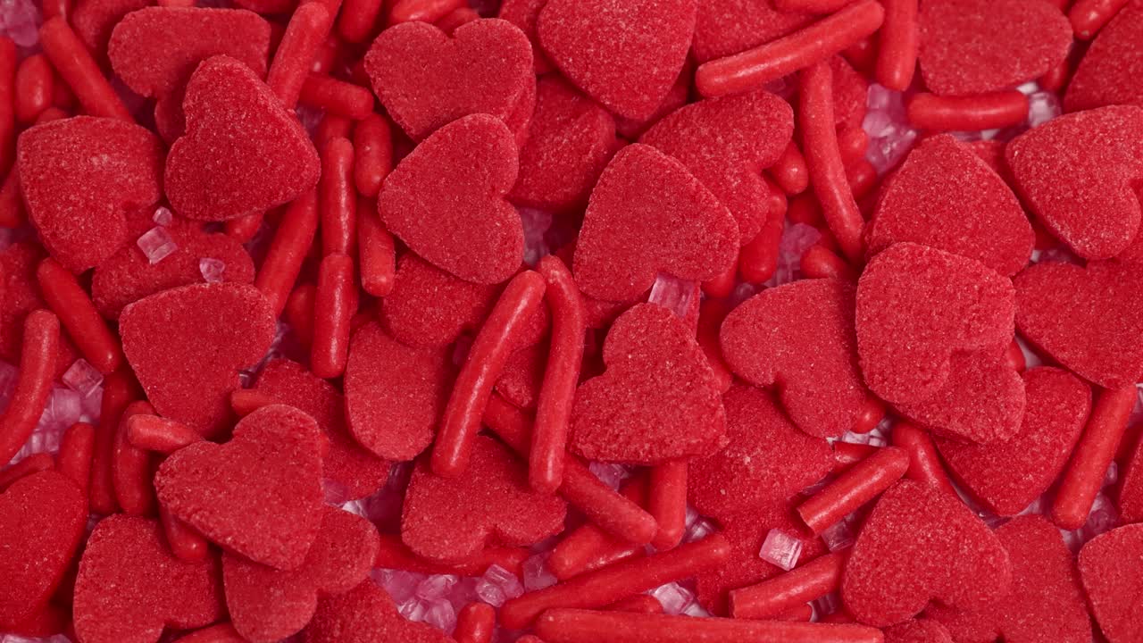 Red heart-shaped candies and sprinkles cascade in a vibrant, close-up shot with consistent lighting and dynamic movement