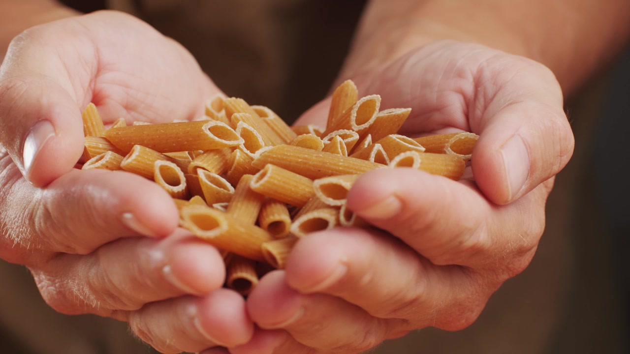 Pasta integrale biologica, maccheroni di semola di grano duro, penne rigate crude in una ciotola di legno. Filmato 4k di alta qualità