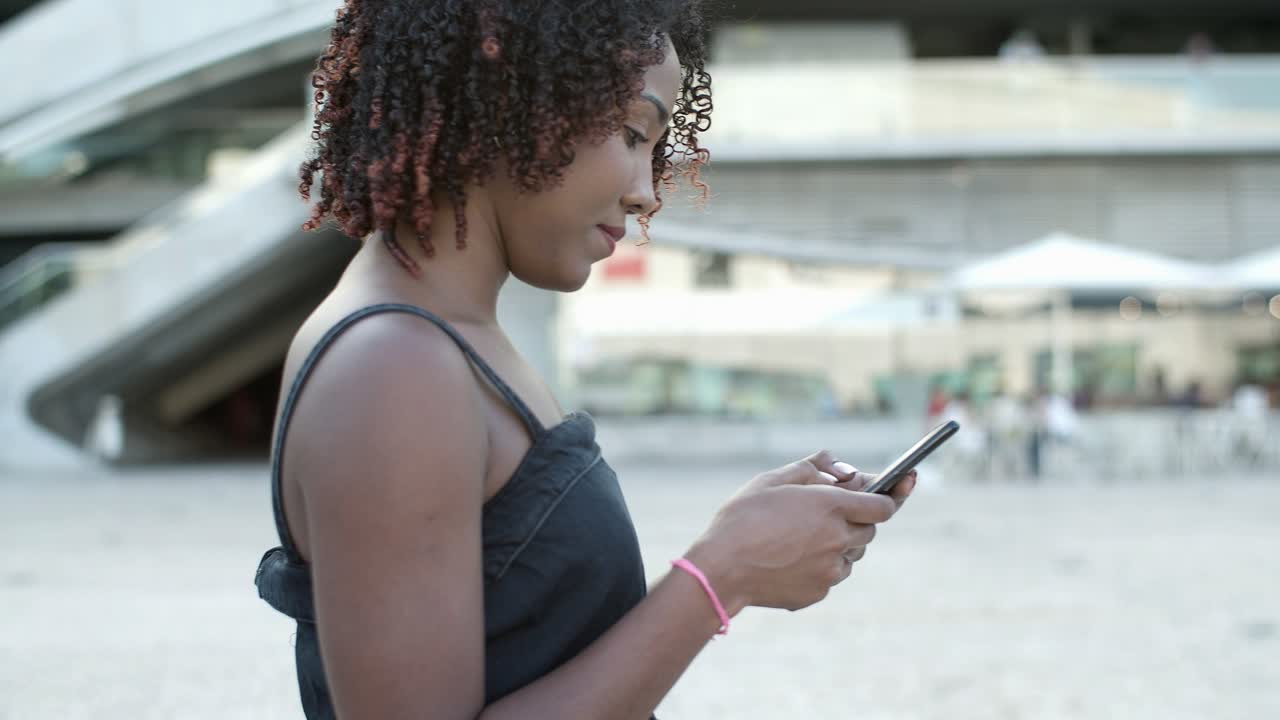 Smiling African American curly woman using phone